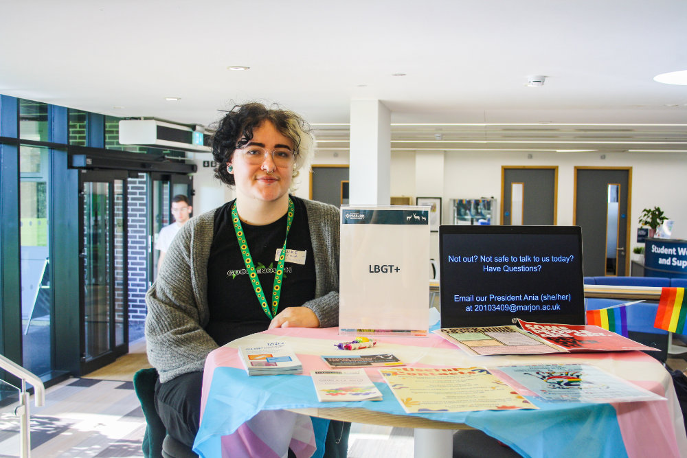 A  student at a table with an LGBTQ society sign
