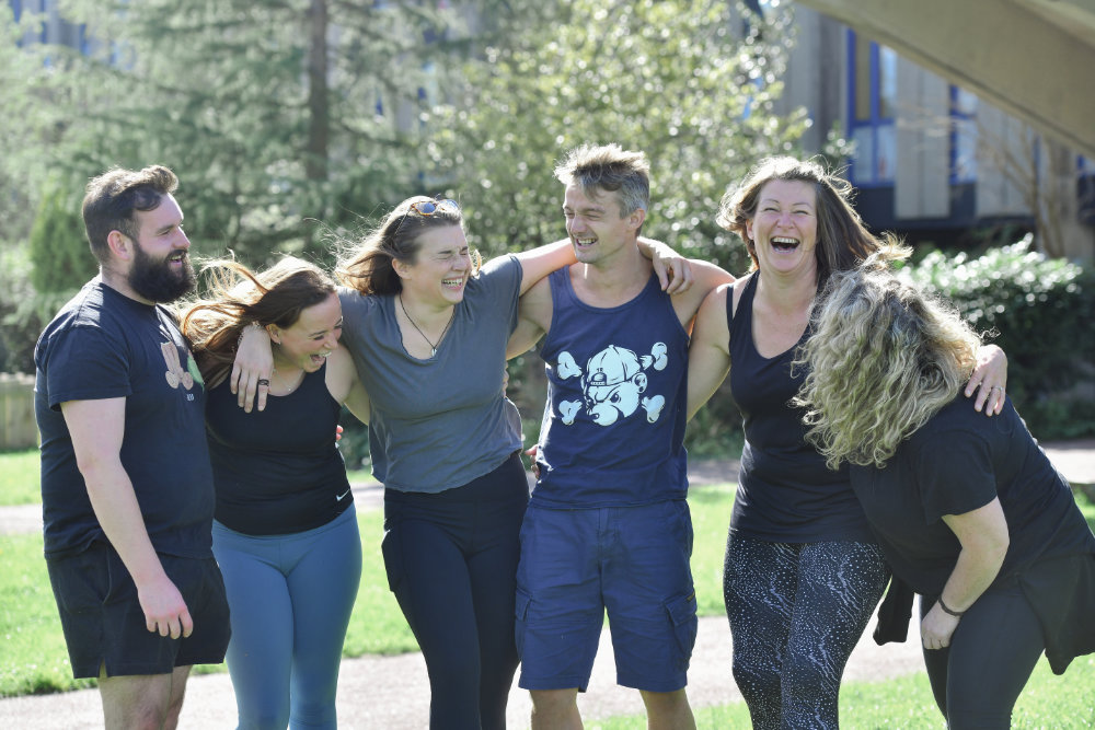Five students standing arm in arm in the  quad and laughing